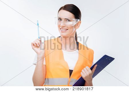 Great perspective. Nice adorable female engineer  gesturing with pen while smiling to the camera  and carrying folder