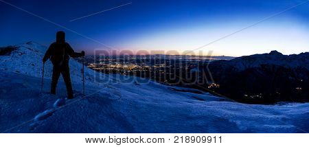 Hiker looking at a winter mountain landscape while the ISS (International Space Station) leaves his trail in the evening sky. North Italy, Europe.