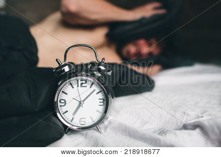 Time to wake up. Tired man in the bed not happy. Mature guy holding alarm clock while checking time for work.
