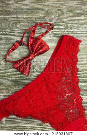 A photo of the red silk bow tie and red lace g- string on the table. Red lingerie. Photo from above