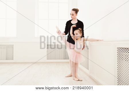 Little girl learning ballet with teacher copy space. Cute small ballerina training classical dance exercises with female coach.