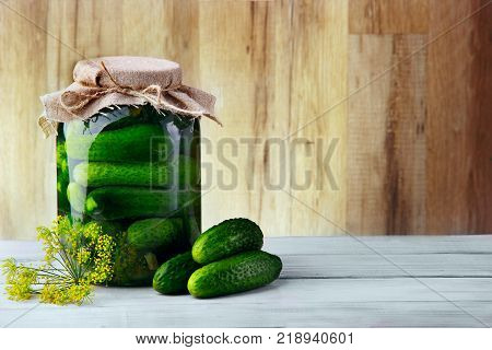 Jar with cucumbers three cucumbers and flower of dill.Wooden background .Free space.Horizontal shot