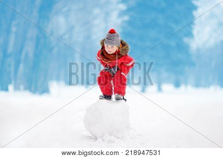 Little boy in red winter clothes having fun with snowball. Active outdoors leisure with children in winter. Kid during stroll in a snowy winter park