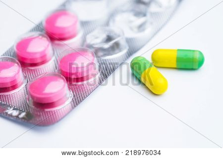 Yellow and green capsule with used magenta tablets medical pills in silver foil pack on white background.
