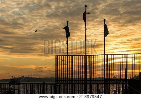 flags and fence of a ferry landing with the skyline of Istanbul in the background at sunset