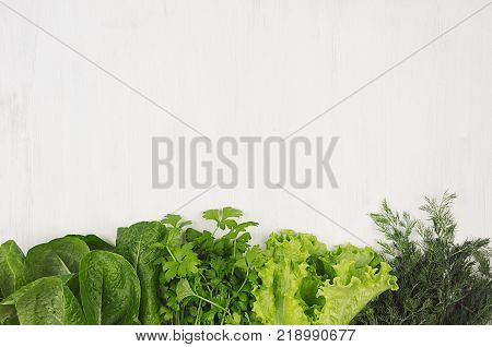 Salad spinach dill parsley sheaves on white wood plank top view decorative border.
