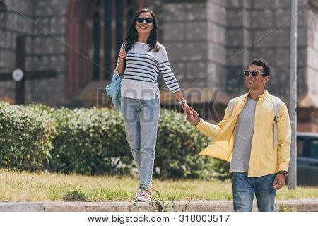 Multiracial Man In Sunglasses With Woman Holding Hands And Walking
