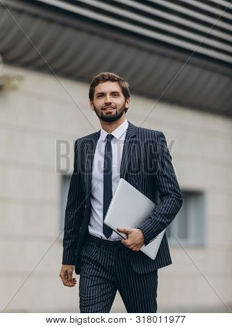Businessman In Suit With  Laptop  In His Hand Goes To Work On The Road To The Entrance Of A Glass Of