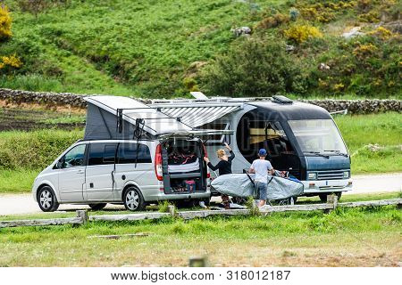 Motorhome Rv And Campervan Are Parked On A Beach. Surfers On Vacation Are Packing Surfboards Or Boar