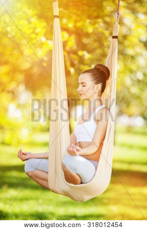 Anti-gravity Yoga outdoor. Happy woman doing yoga exercises, meditate in sunny park. Yoga meditation in hammock. Concept of healthy lifestyle and relaxation. Pretty woman relax at yoga hammock