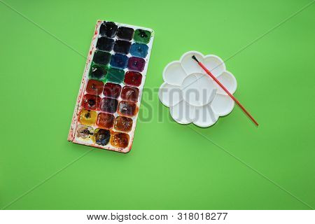 Brush, Paint, Palette To Mix On A Green Background. Watercolor And Colored Objects For School And Cr