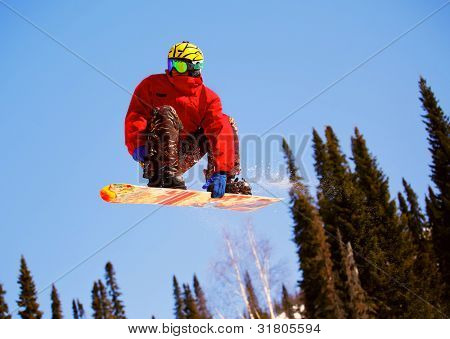 Snowboardista skoky vzduchem s tmavě modrou oblohou v pozadí