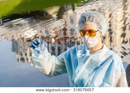 Female Epidemiologist Demonstrates A Test Tube With Water Against The Background Of A Water Surface 