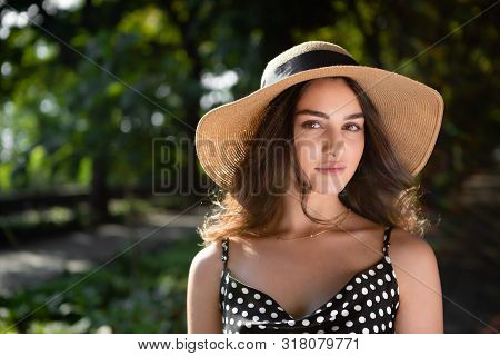 Close-up Porttrait Of A Beautiful Young Brunette Woman Dressed In A Black Dress And A Hat With Wide 