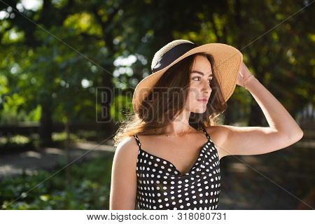 Close-up Porttrait Of A Beautiful Young Brunette Woman Dressed In A Black Dress And A Hat With Wide 