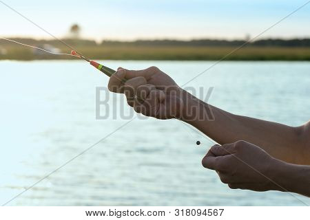 Fisherman With A Rod In Hands Is Adjusting The Depth By Fishing Float.