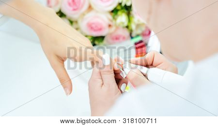 Hands of a skilled manicurist working on fingernails of a young woman