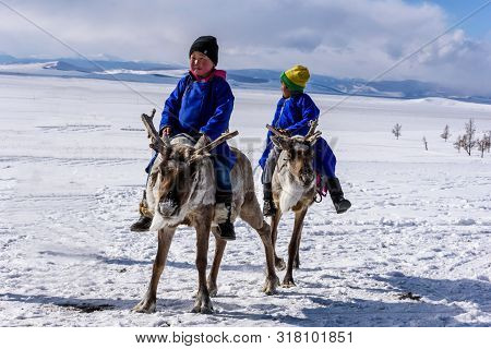Hatgal, Mongolia, Febrary 25, 2018: Little Tsaatan Boys In Traditional Mongolian Riding On Reindeers