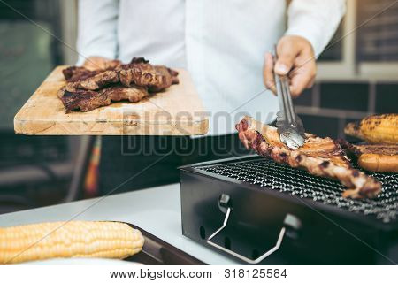 Asian Men Are Pinching The Pork Ribs On The Grill And Holding Them To Friends Who Are Celebrating In