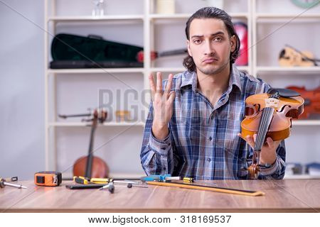 Young handsome repairman repairing violin