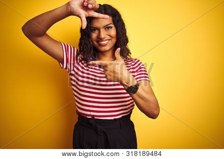 Transsexual transgender woman wearing stiped t-shirt over isolated yellow background smiling making frame with hands and fingers with happy face. Creativity and photography concept.