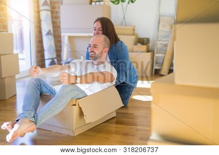 Funny and crazy couple having fun riding a cardboad box as a car, smiling happy and lauging at new home