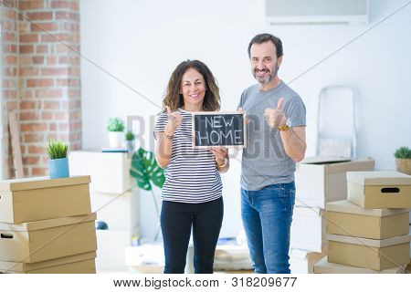 Middle age senior couple holding blackboard moving to a new home happy with big smile doing ok sign, thumb up with fingers, excellent sign