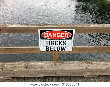 Thetis Island, Canada - July 13th, 2019: A Sign On A Dock High Up Reading Danger Rocks Below With Th