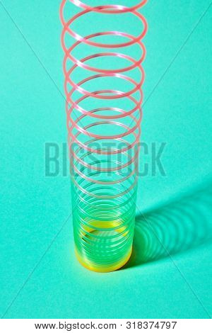 Multicolored slinky toy spiral with soft shadows on a pastel turquoise background, place for text.