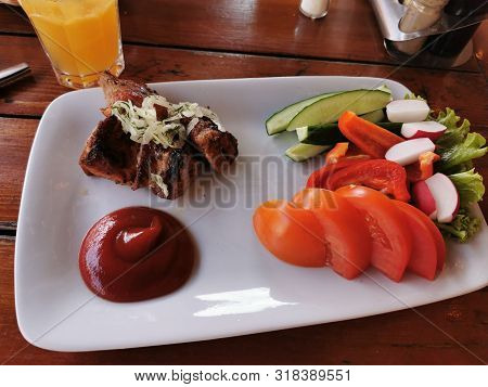 Barbecue, Pieces Of Pork Cooked On Coals And Sliced Vegetables - Cucumbers, Tomatoes, Salad On A Whi
