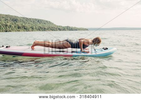 Middle Age Caucasian Woman Practising Yoga On Paddle Sup Surfboard At Sunset. Female Stretching Doin