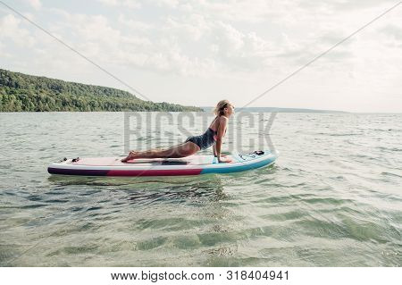 Middle Age Caucasian Woman Practising Yoga On Paddle Sup Surfboard At Sunset. Female Stretching Doin