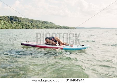 Middle Age Caucasian Woman Practising Yoga On Paddle Sup Surfboard At Sunset. Female Stretching Doin