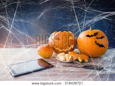 holidays, halloween and technology concept - jack-o-lantern or carved pumpkin, tablet pc computer, knife on wooden table and spiderweb over starry night sky background
