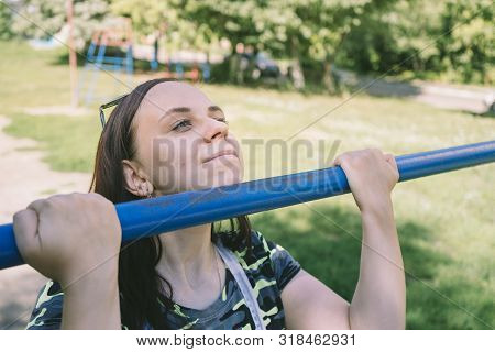 A Young Handsome Woman In Casual Clothes Is Doing Pull Up Exercise On Horizontal Bar. Fitness, Sport