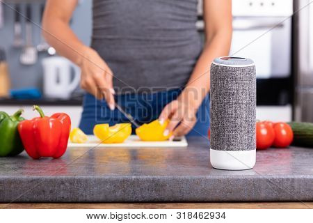 Close-up Of A Woman Working In Kitchen With Smart Speaker In Foreground