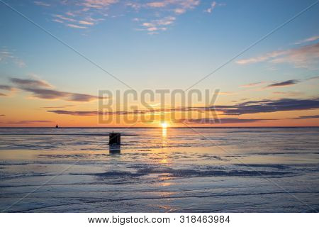 The sun setting over a frozen harbor and an ice fishing shack in rural Prince Edward Island, Canada. Lighthouse on the horizon.