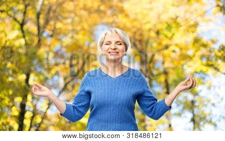 zen, relax and old people concept - portrait of smiling senior woman in blue sweater chilling over autumn park background