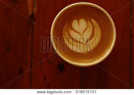 Hot Cup Of Coffee With Fern Latte Art In A Paper Cup On A Red Timber Coffee Table From Above