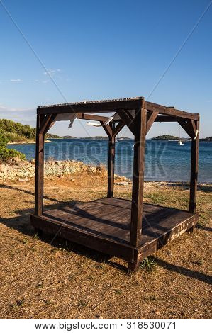 Empty Wooden Construction, Used As A Lounger. Beach With Mixed Soil And Sand. Water Of The Adriatic 