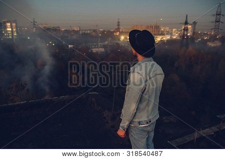 Urban Man With Hat Against The Background Of The City. Wearing White Shirt And Jeans. Old Neglected 