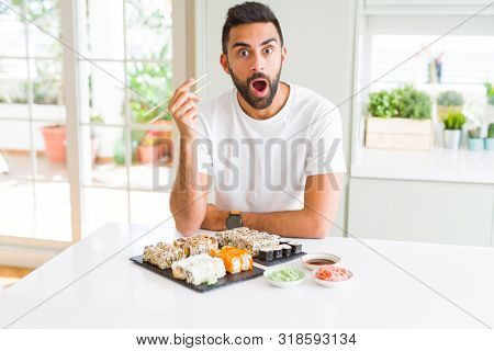 Handsome hispanic man eating asian sushi using chopsticks scared in shock with a surprise face, afraid and excited with fear expression