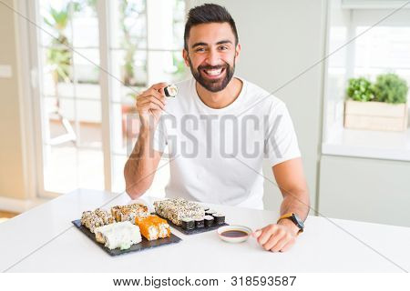 Handsome man smiling happy enjoying eating fresh colorful asian sushi using chopsticks