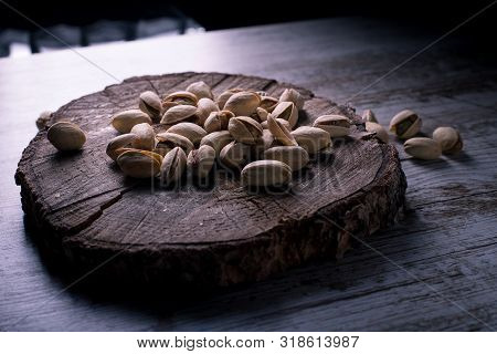 Pistachios On Wooden Table In The Foreground With Darkened Background