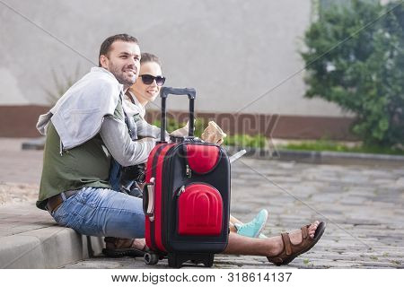 Happy Couple Traveling Around City. Having Lunch With Sandwiches. Sitting On Floow With Luggage And 
