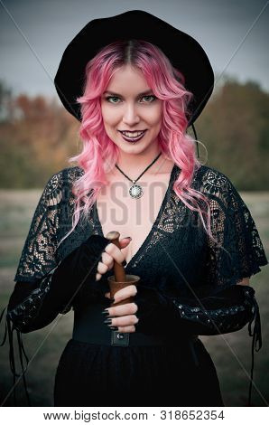 Halloween Theme: Modern Smiling Young Witch In Black Dress And Hat With Mortar And Pestle In Hands