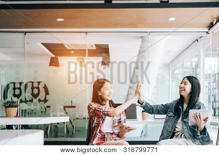 Young Studebt Sitting In Library Studying Sharing Knowledg And Giving High-five While Their Colleagu