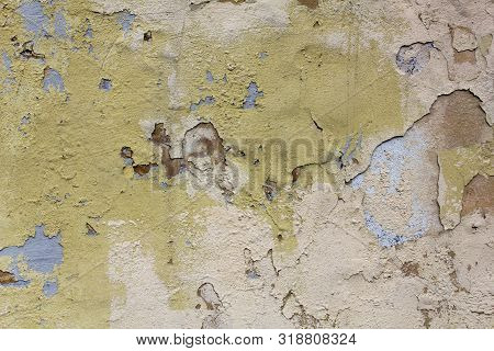 Old Damaged White Yellow Wall With Peeling Brown And Blue Paint. Rough Surface Texture