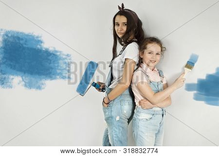 The Girls Paint The Walls. Friendly Collaboration Between The Two Sisters. Teens In Blue Overalls Ma