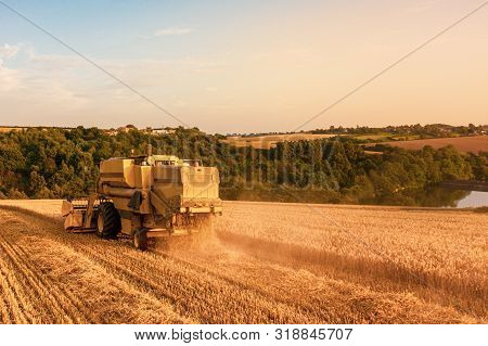 Rear Aerial Shot Of A Combine Harvester Harvesting A Wheat Field At Sunset In The Uk
